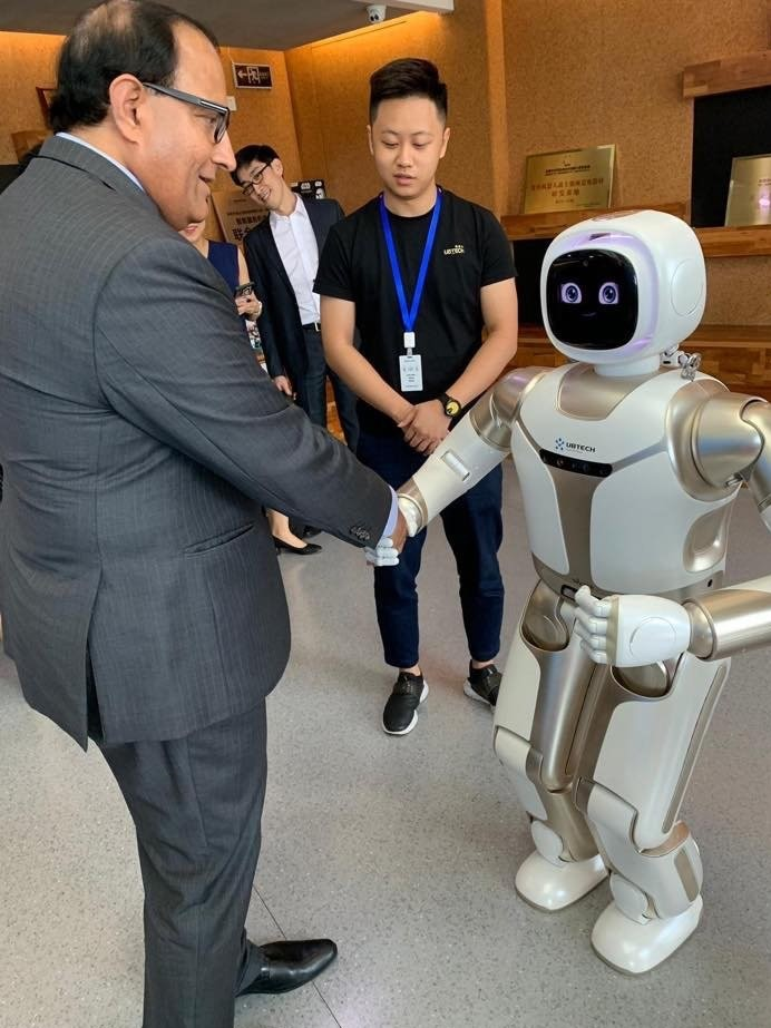 Man in suit shaking hands with a white and silver UBTECH robot with a screen displaying eyes.